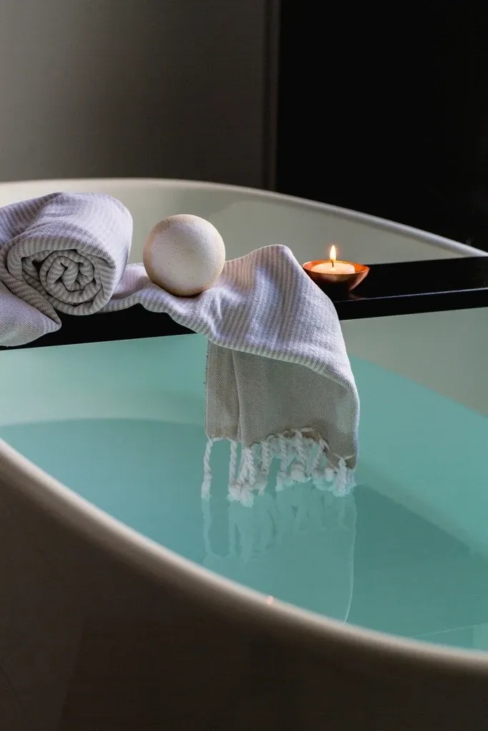 A rolled towel and a candle by a calm bath