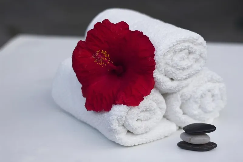 Rolled white towels with a red flower and stones